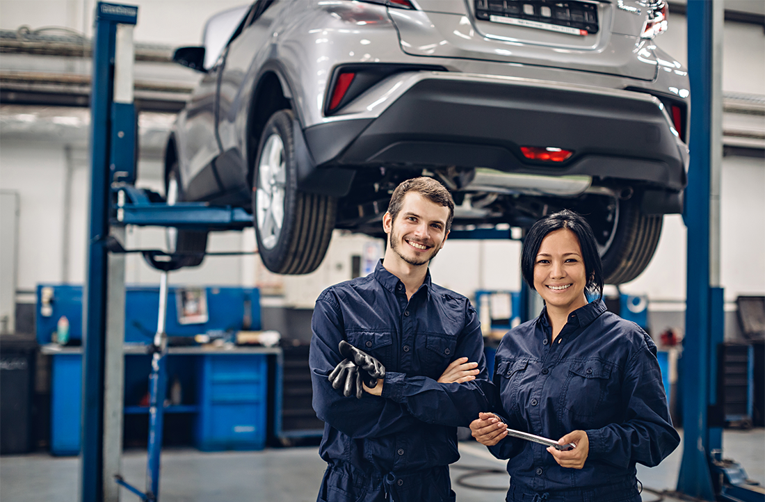 Two auto repair technicians in front of a car on jack stands.