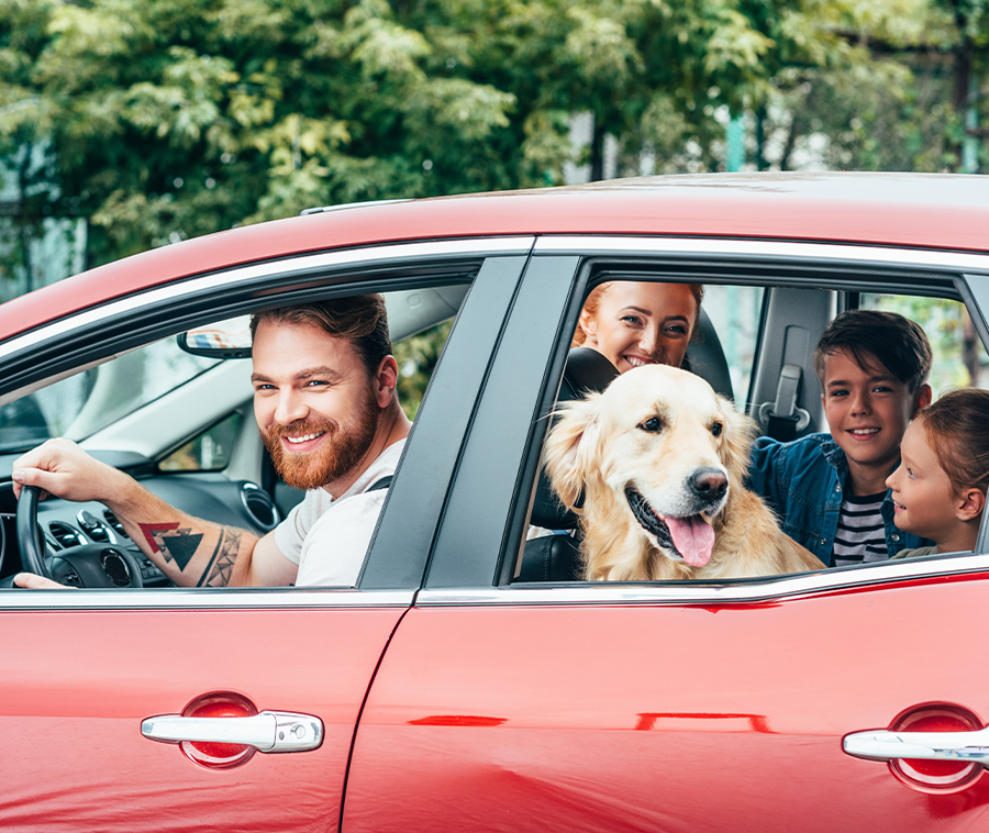 Tips for Auto Insurance Buyers in 2024: A family in a red four-door sedan getting ready for a family trip.